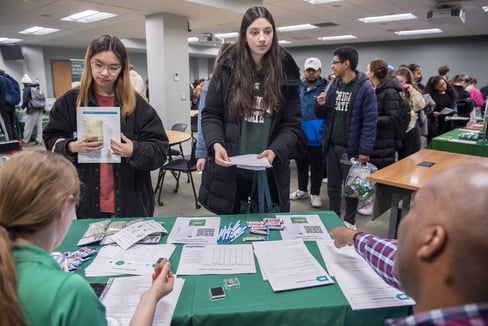 A man and a woman at a booth share information with students.