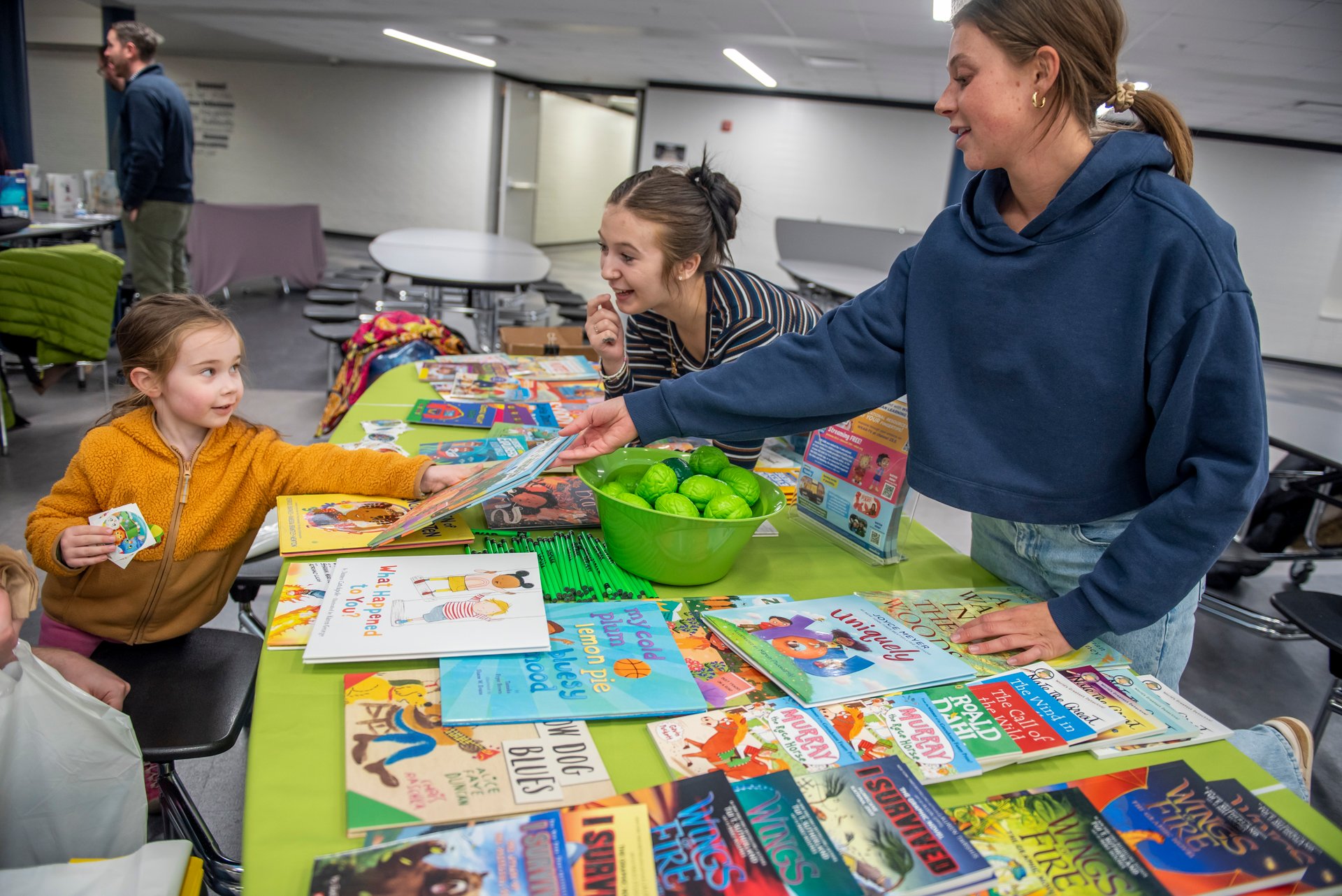 Woman hands a child a book.