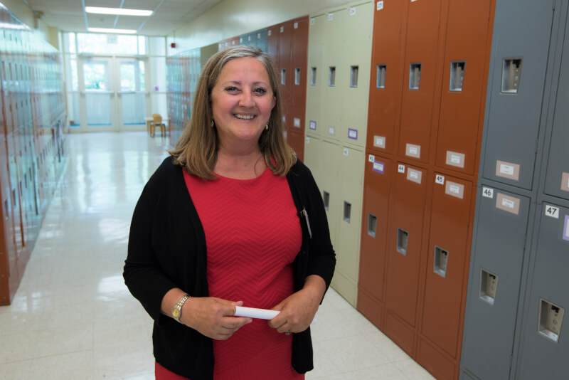 Woman stands smiling in front of lockers.