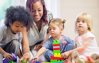 Two year olds and an adult play with blocks.