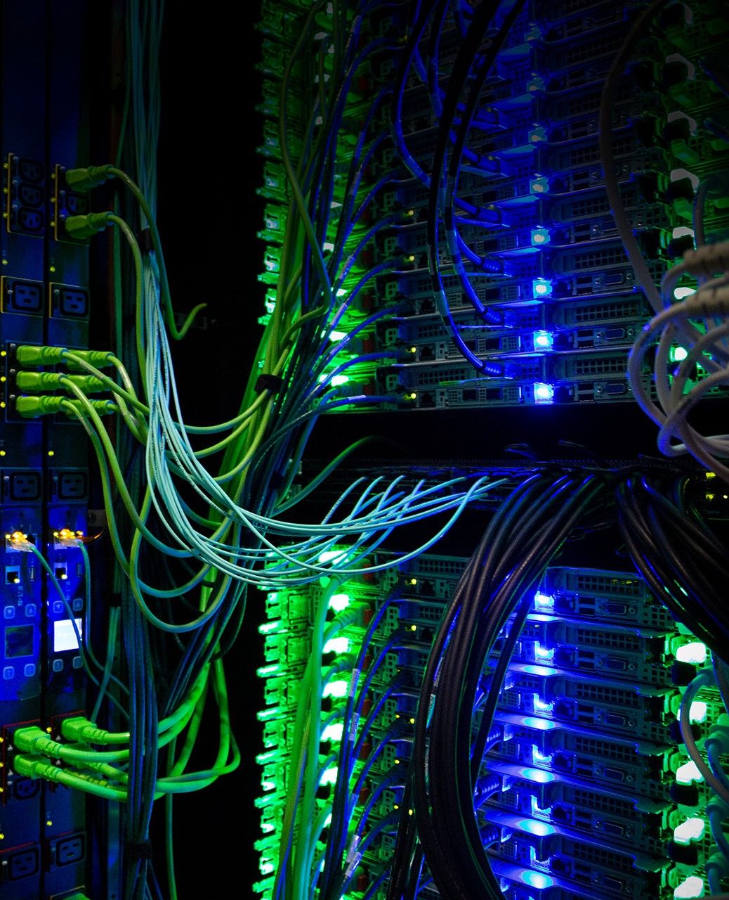 Supercomputer hardware with blue and green lights and many wires connect it together. 