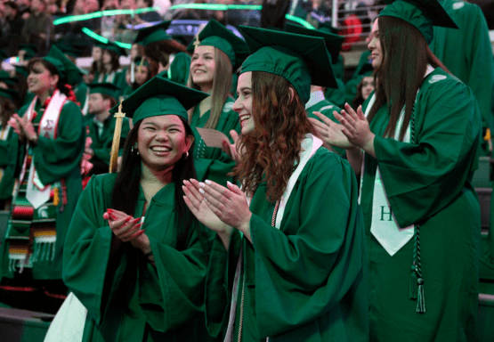Group of James Madison college graduates clapping and smiling during the college's annual commencement ceremony.
