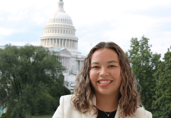 JMC student wearing a white blazer posing in front of the Washington Capitol building.