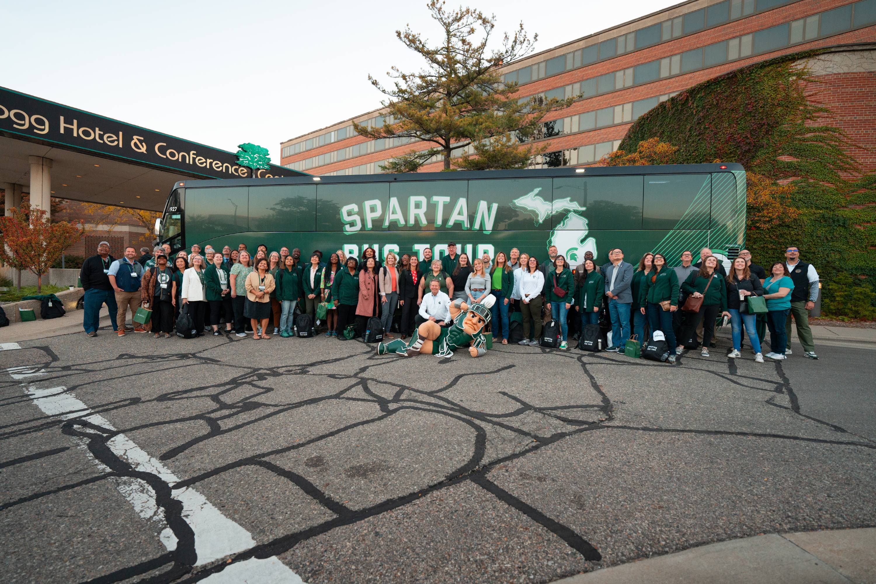 Group photo of Spartan Bus Tour participants in front of the bus outside the Kellogg Center.