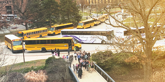 School buses lined up in the driveway in front of Wharton Center and students walking up the sidewalk towards the building