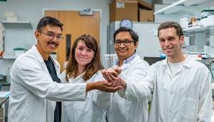 MSU employees in lab coats smile at the camera with their hands extended.