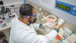 A man in a white lab coat works at a laboratory bench.
