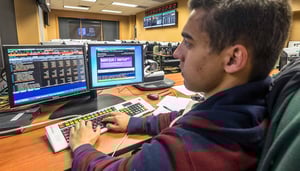 A man types while looking at two monitors while sitting at a desk.