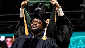 Graduate stands on-stage while a stole is placed on their shoulders.