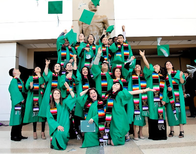 Students toss graduation caps in the air in front of the Spartan Statue in Spartan Stadium.