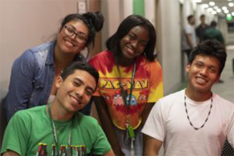 A group of students gathered together in center frame all smiling while looking at the camera.