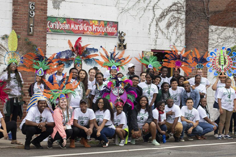 A large group of TRIO students stand in front of a brightly decorated and designed wall outside of a building.