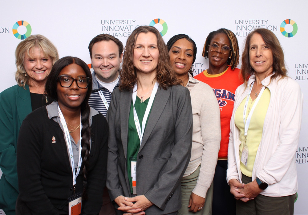 A group of people standing closely together smiling at the camera backdropped by the UIA Summit backdrop