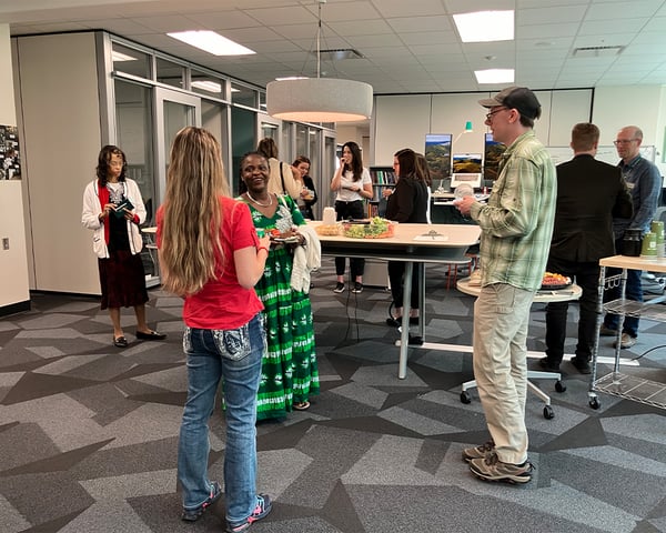Several people are spread across an open workspace socializing during the CTLI Open House.
