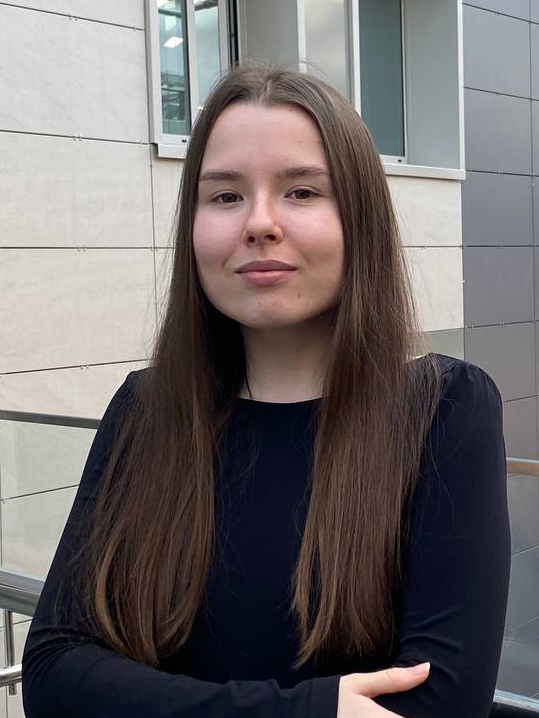 Rimma Korchmit stands smiling with arms crossed, wearing a black top and blue bottom