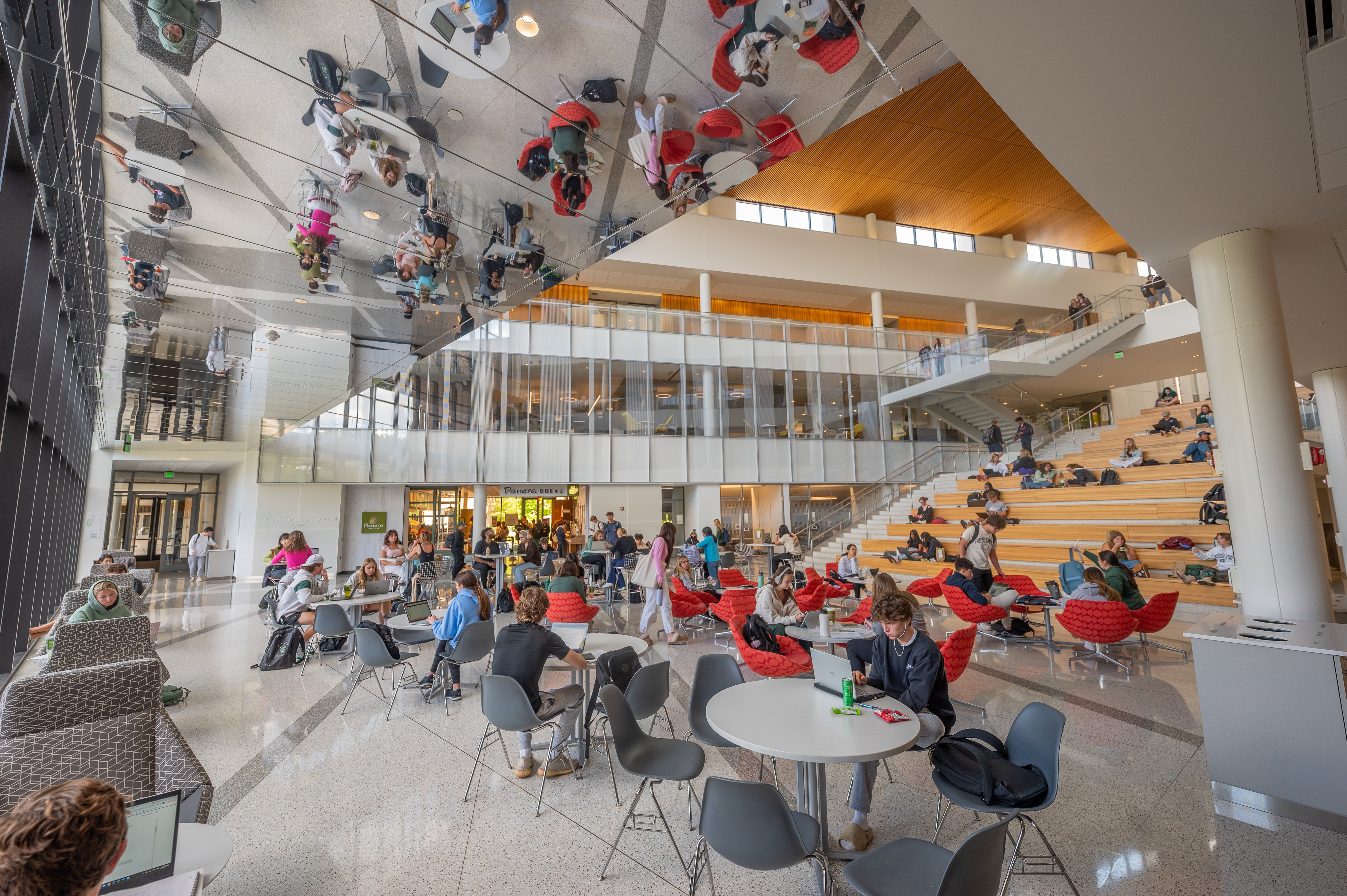 Students gather within the business college on the stairs and at the tables in the main atrium.