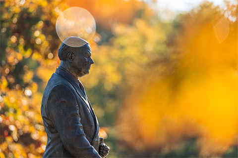 Top portion of the John Hannah statue outside of MSU's Administration Building, foregrounded by fall foliage and colors. 