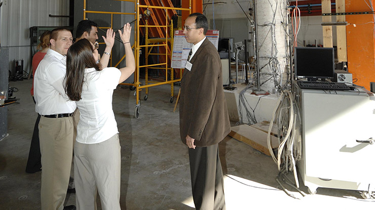 Students pursuing a civil engineering degree converse in a big, industrial space full of civil engineering equipment.