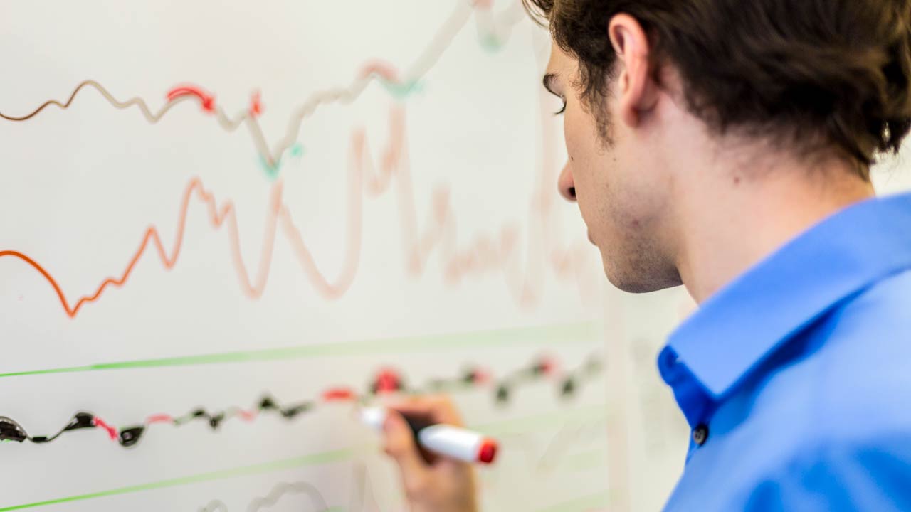 A finance major at MSU draws a graph on a dry erase board.