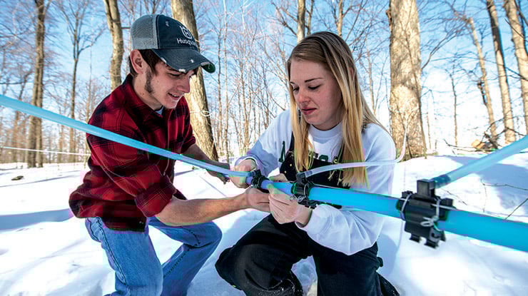 Students working toward a forestry degree assemble forestry equipment outdoors on a bright, snowy day.