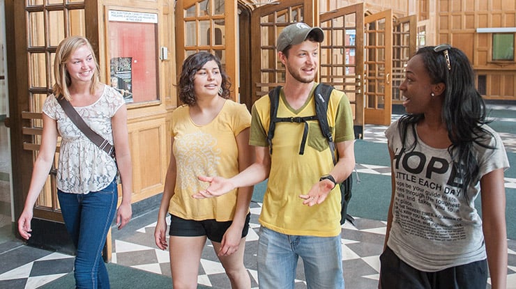 A group of smiling humanities majors walk side by side down a hallway in a building on MSU?s campus.