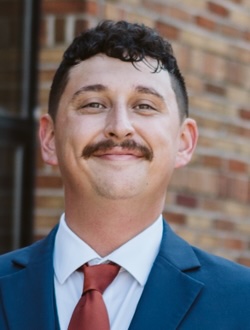 Jake Kilby, MSU turfgrass management alumnus, smiles in a suit and tie outside a brick building.