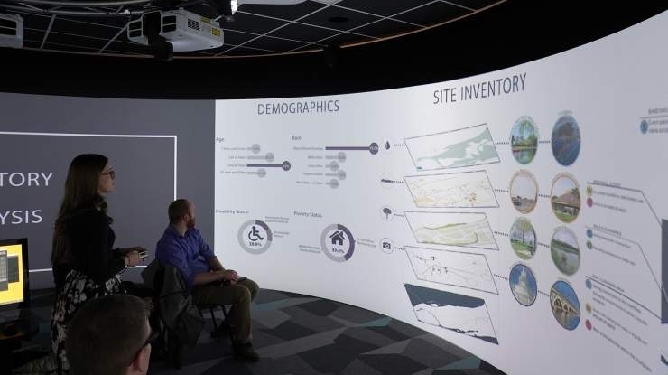 Students working on a landscape architecture degree review site inventory and demographics in a 360? visualization space.