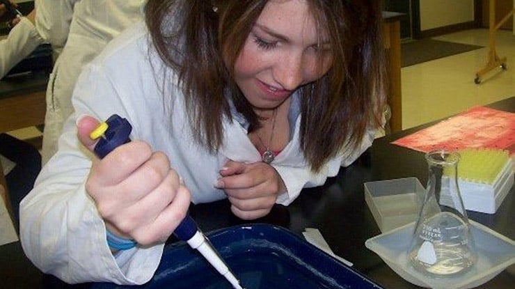 A student pursuing a medical laboratory science degree works in a lab wearing a white lab coat.