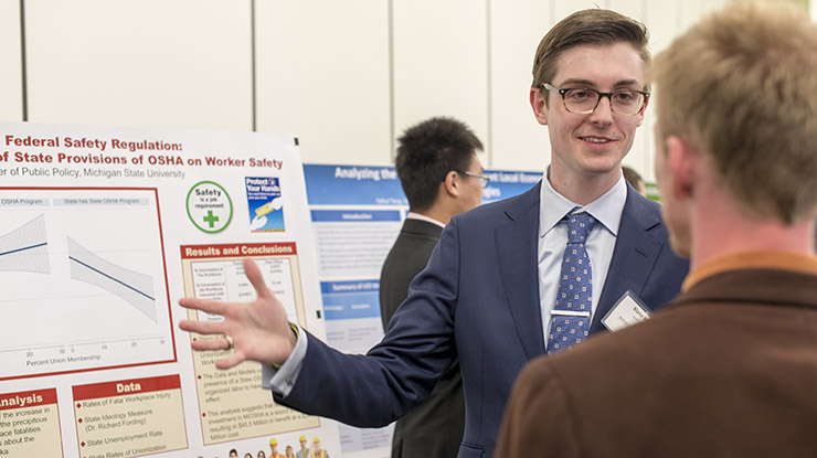 A public policy major presents information next to a board about worker safety and federal safety regulations.