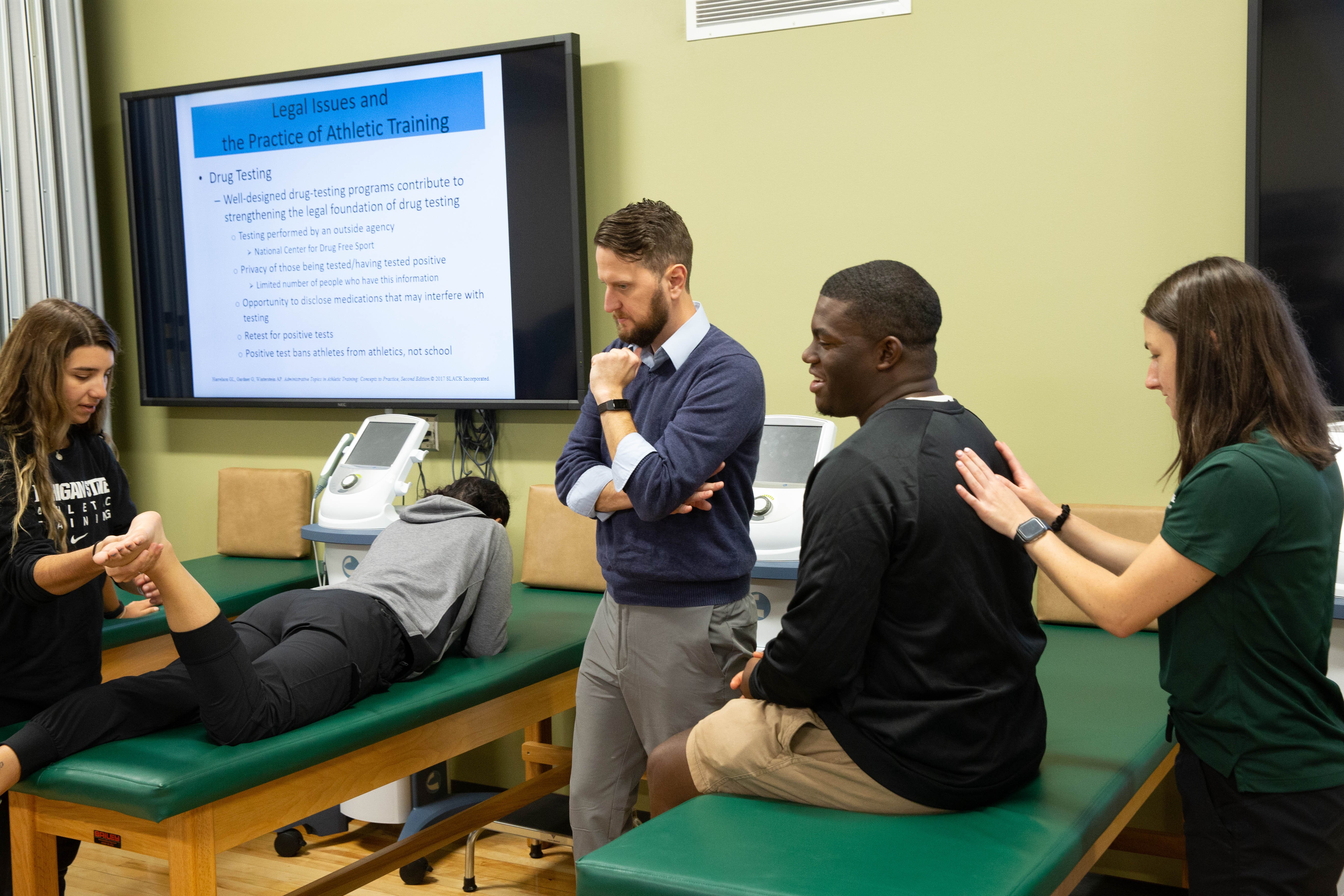 Students practice in a kinesiology lab under the guidance of their professor.