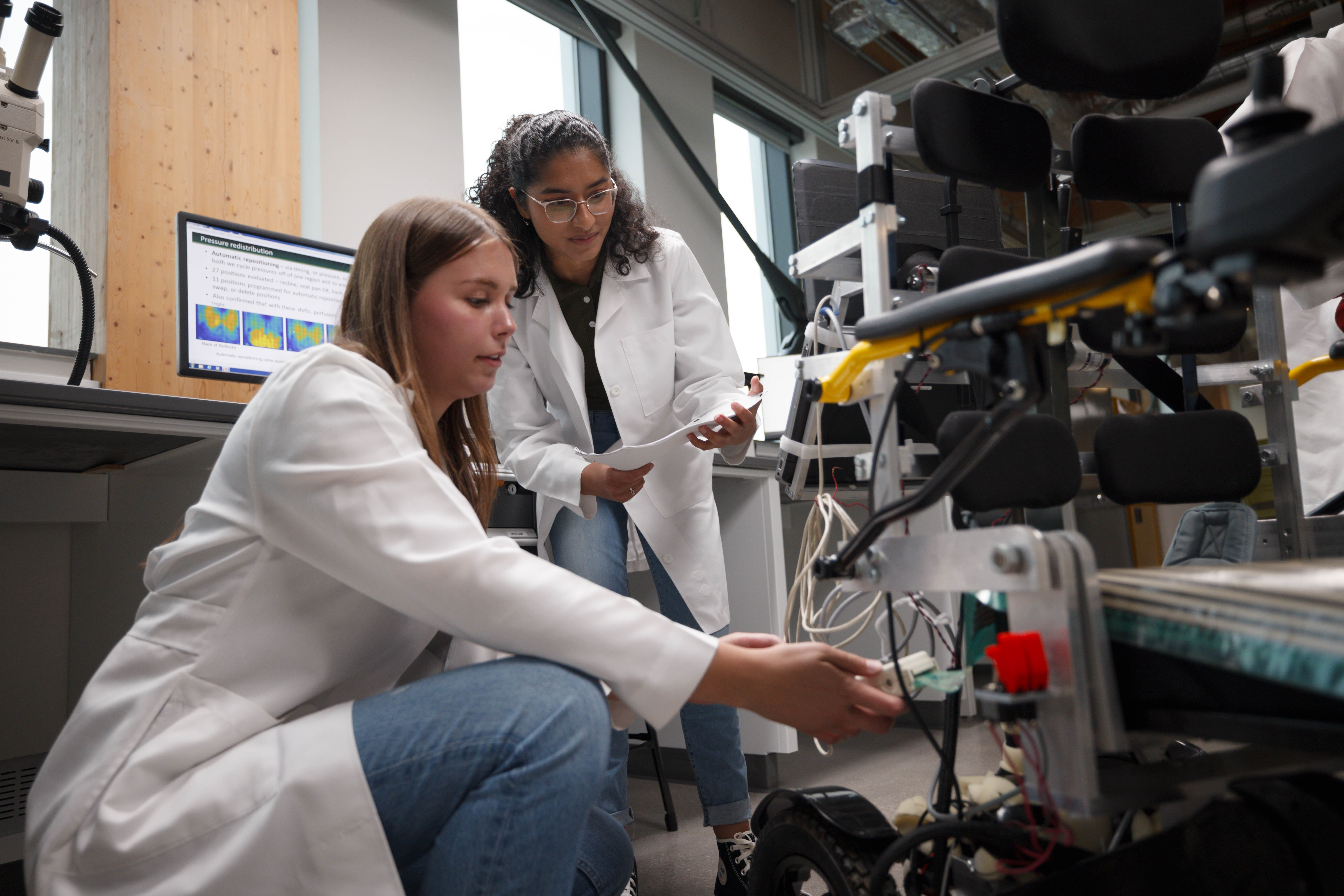 Two students in white lab coats work with STEM equipment.