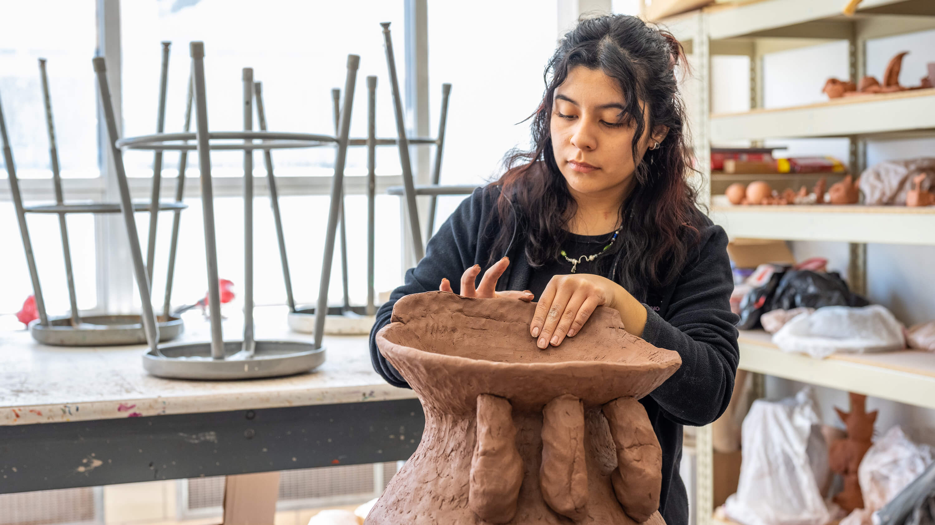 A student shapes a sculpture with their hands at the MSU art center.