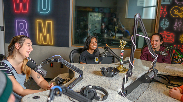 Three MSU students talk into microphones in the student radio station studio.