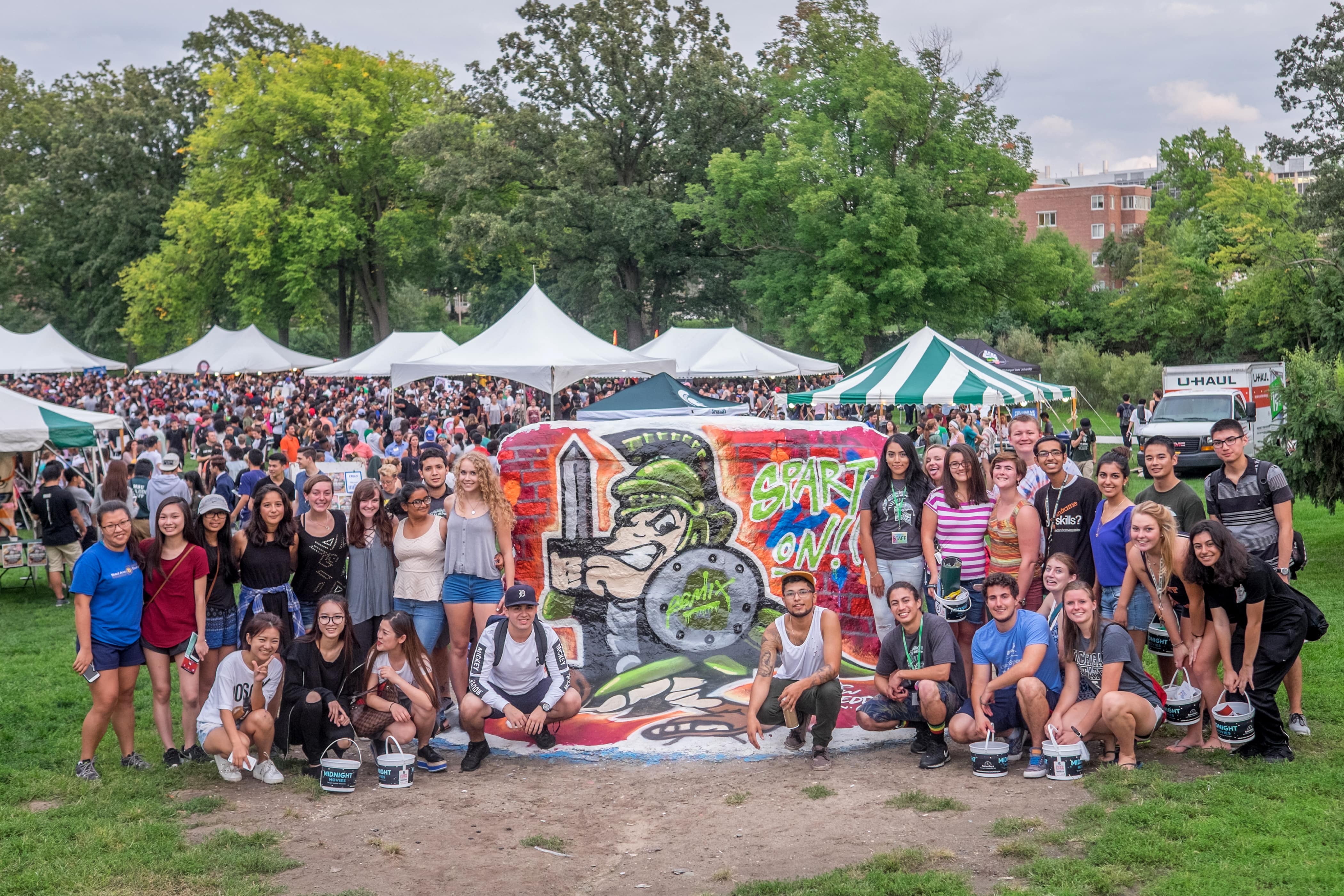 A group of students gathers in front of the rock, posing for a photo, on Michigan State University's campus