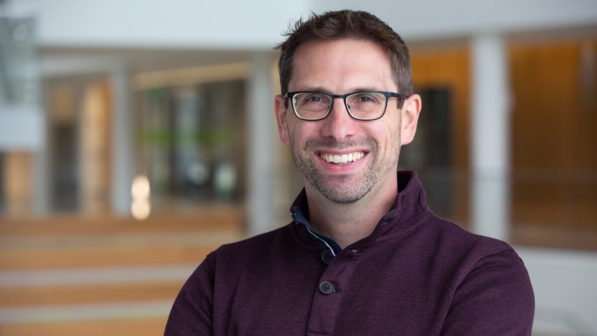 Headshot of Jeremy Van Hof, smiling, wearing a dark shirt and glasses.
