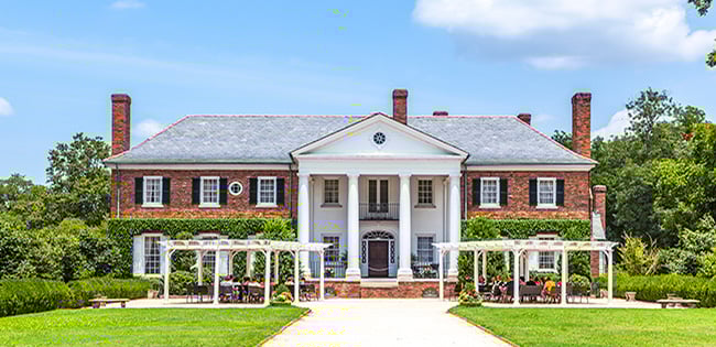 A stately Southern plantation-style mansion in Charleston, South Carolina, with manicured gardens and white pergolas lining the path to the entrance.