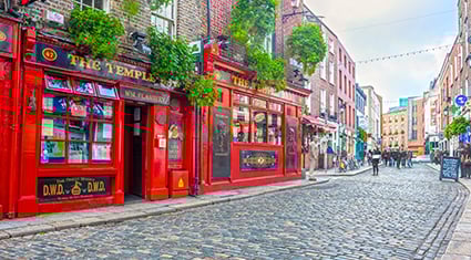 The lively cobbled streets of the Temple Bar district in Dublin, Ireland, with bright red pubs and pedestrians enjoying the vibrant atmosphere.