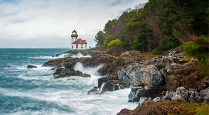 Waves crash against the rocky coastline near Lime Kiln Lighthouse on San Juan Island, framed by evergreen trees and dramatic ocean scenery.