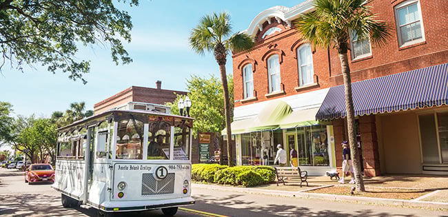 A classic white trolley rolls past historic brick buildings and palm trees in the coastal town of Fernandina Beach on Amelia Island, Florida.
