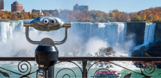 Viewing binoculars overlooking the American Falls at Niagara Falls with autumn trees and city skyline in the background