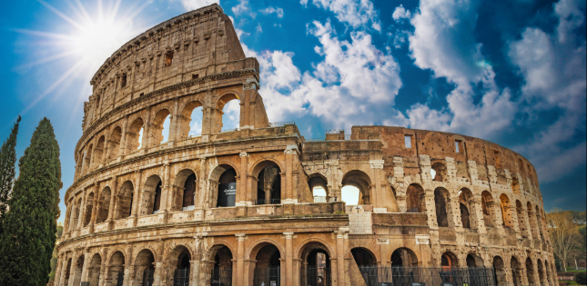 Ancient stone arches of the Colosseum rising against a bright blue sky in Rome, Italy.