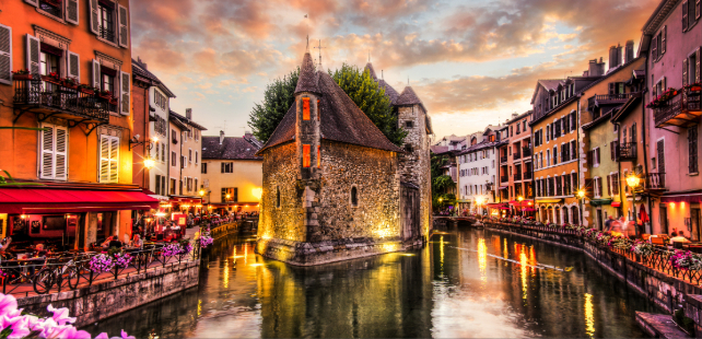 Historic stone Palais de l’Isle building surrounded by canal and colorful buildings in Annecy, France.