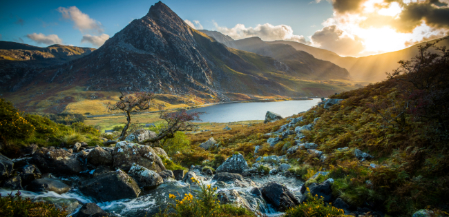 Rocky stream flowing through a valley with Llyn Ogwen lake and Tryfan mountain at sunrise in Snowdonia, Wales.