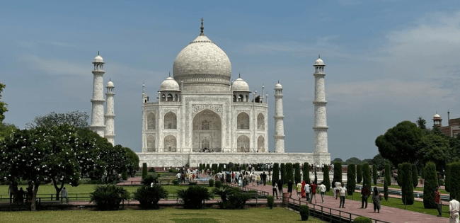 Taj Mahal viewed from the front, with visitors walking through the gardens and pathways leading to the monument.