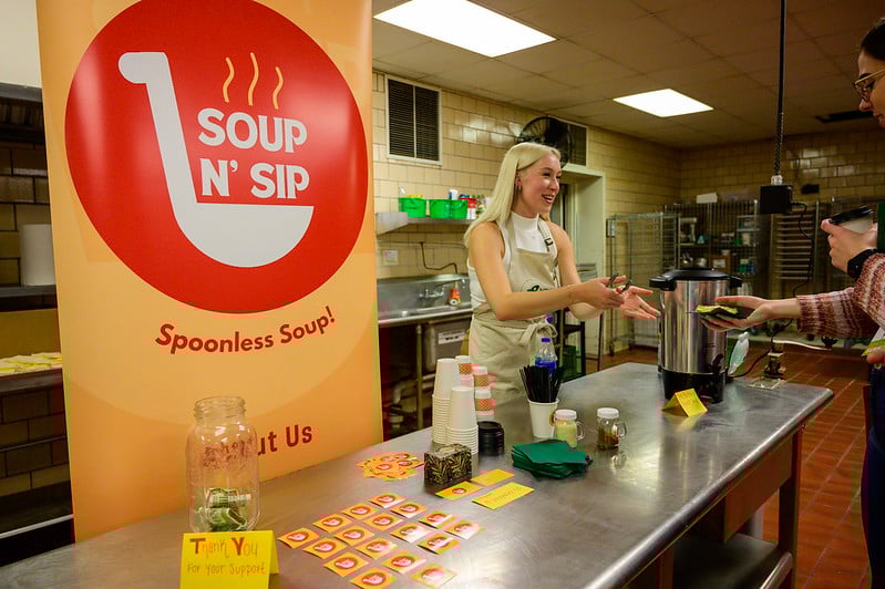 Woman handing out soup samples from her Soup N' Sip in the Venture Kitchen.