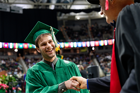 Smiling student at graduation ceremony shaking administrator's had while walking across the stage.