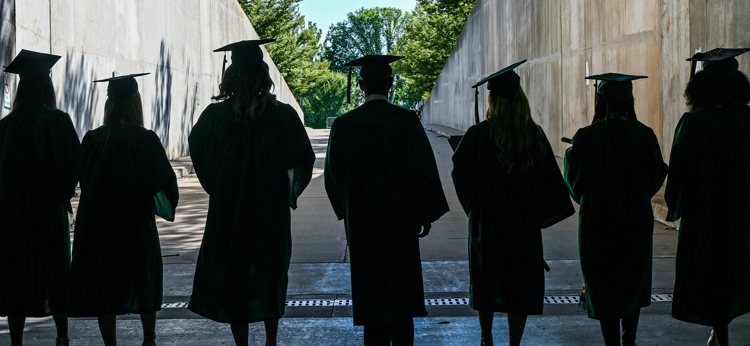 Students in graduation gowns walking through dark tunnel