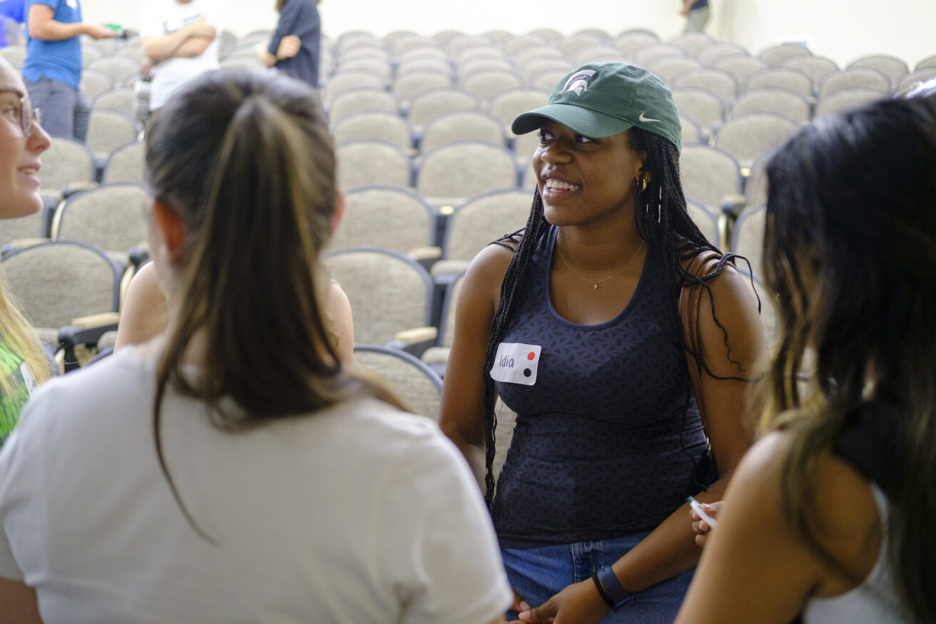 Women econ majors talking in a lecture hall. 