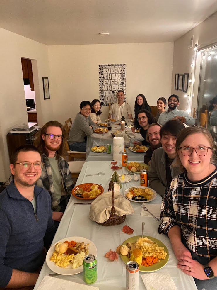 Graduate students smile around a table filled with food during friendsgiving.