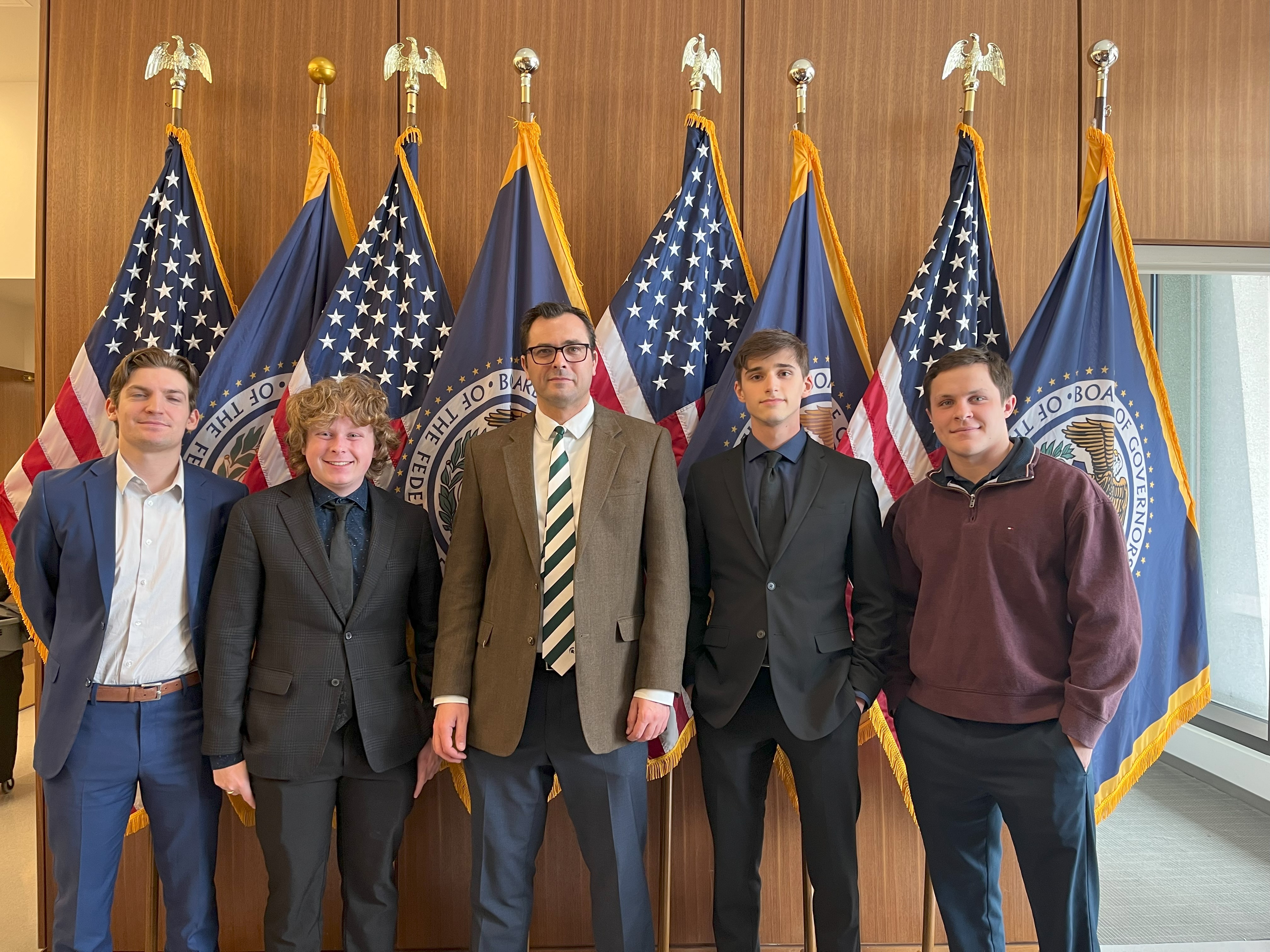 One professor and four students stand in front of flags. 